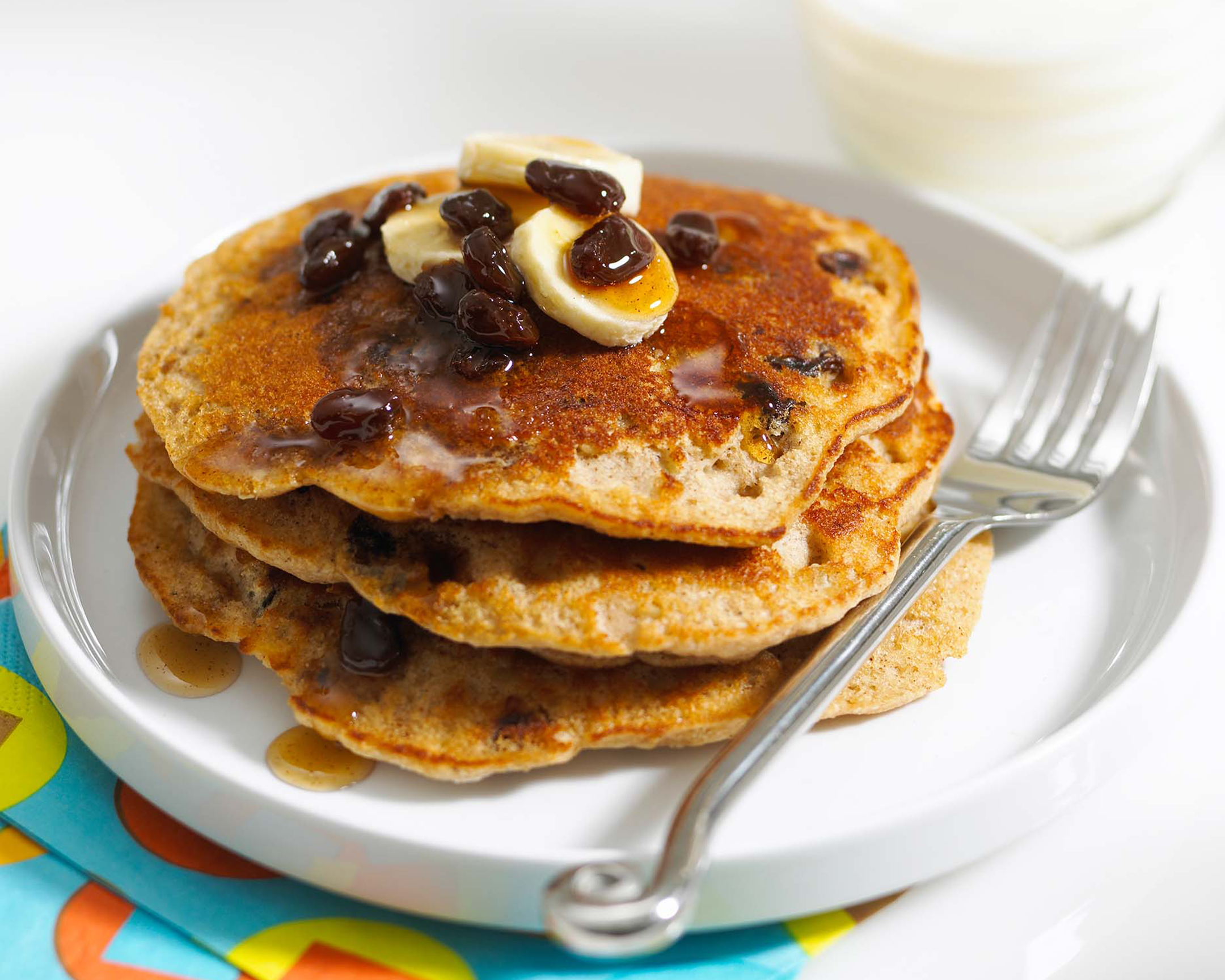 pancakes with butter and syrup and raisins on a white plate with a fork